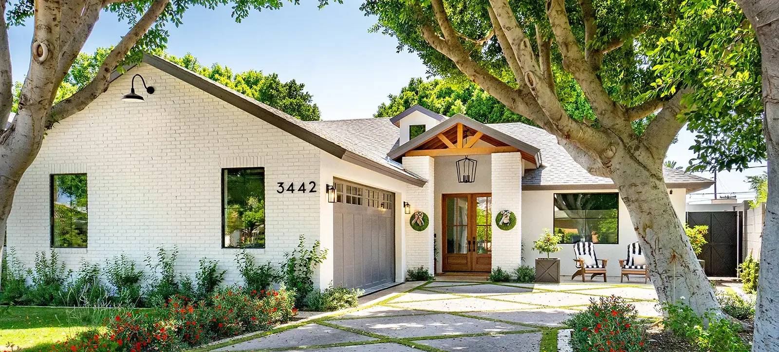 White brick ranch-style home with wood-beam gable entry, paver driveway, and mature trees.
