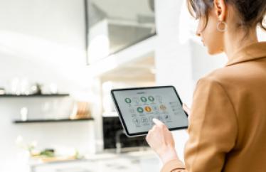 Woman in an orange shirt touches the screen of an iPad that is showing a smart thermostat application.