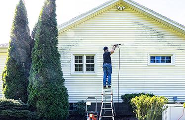 homeowner power washing their home's exterior while standing on a ladder