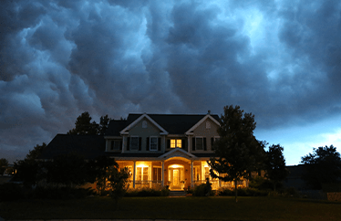 home in the evening with lights on and stormy clouds hovering above it